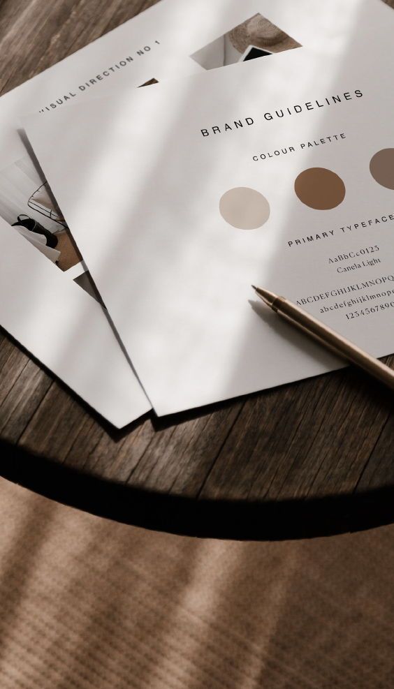 Documento de brand guidelines com paleta de cores e tipografia, ao lado de uma caneta dourada.